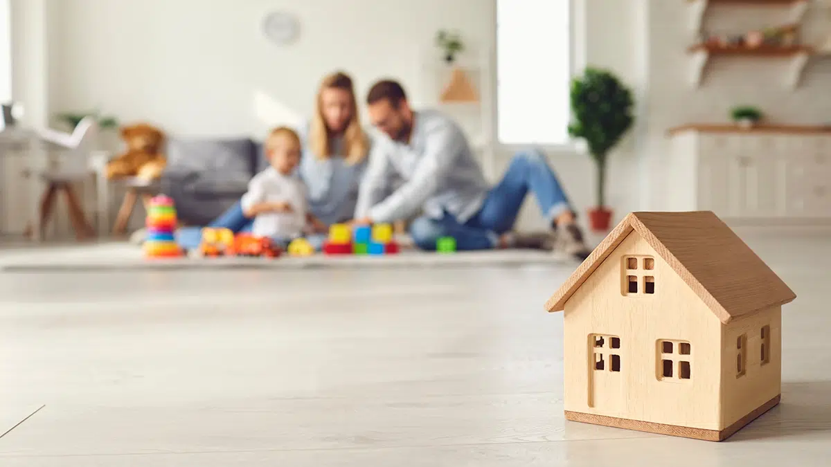 Famille heureuse avec bébé en arrière-plan flou et maison en bois miniature au premier plan